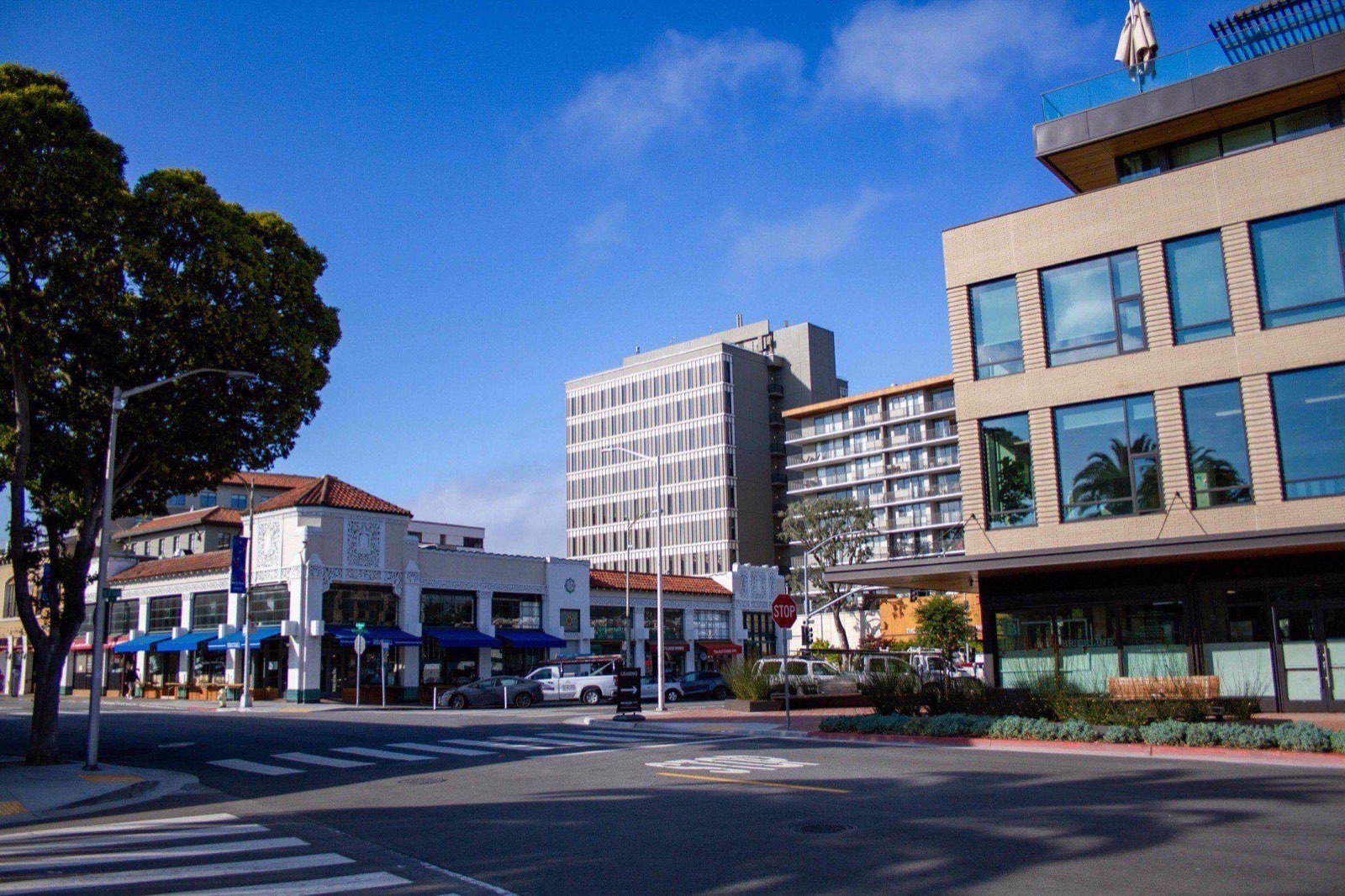 A downtown San Mateo corner: low Spanish-revival storefronts with awnings, a 1960s office tower behind them, and a new mixed-use block opposite