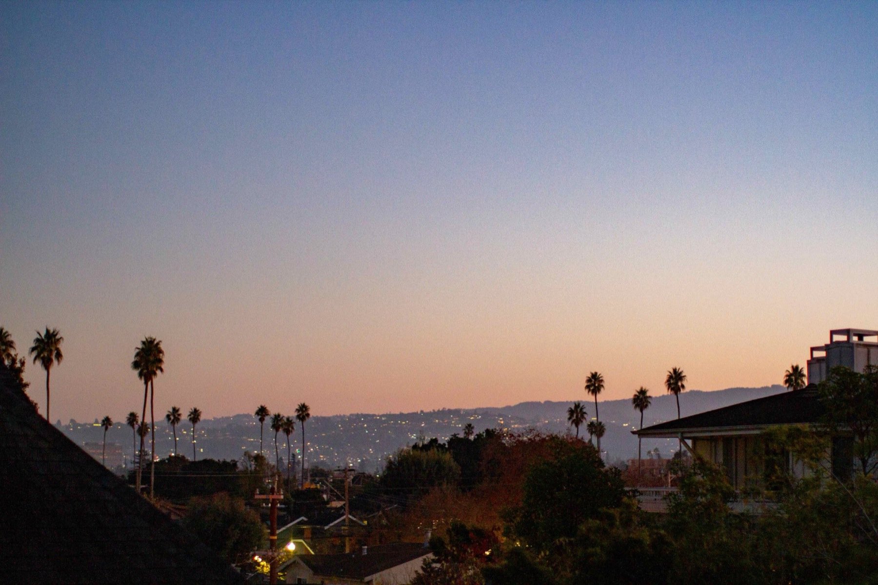 The hills west of San Mateo at dusk, house lights scattered across the ridge above rooftops and palm trees